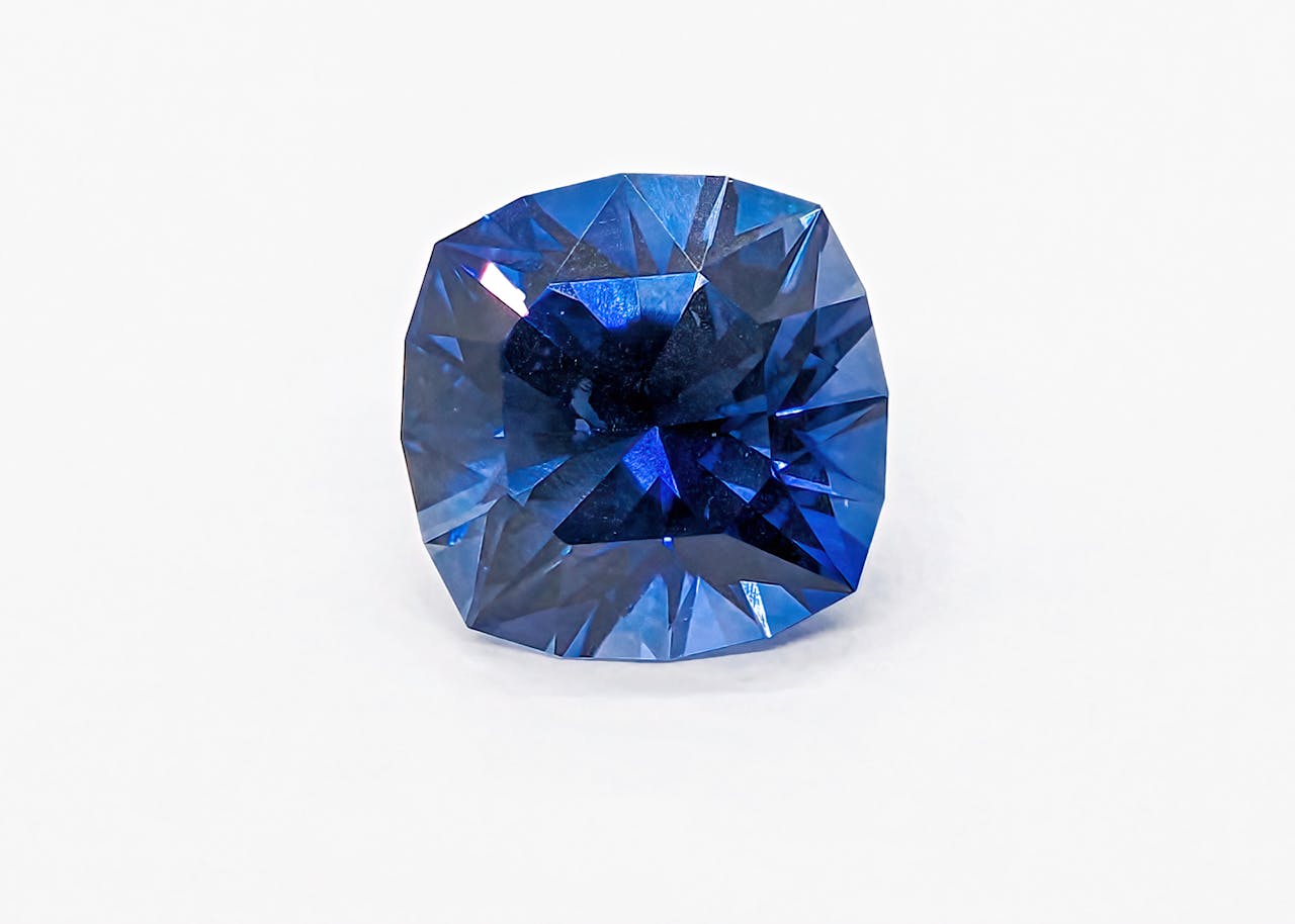 A vivid blue sapphire gemstone on a white background, showing its intricate facets.