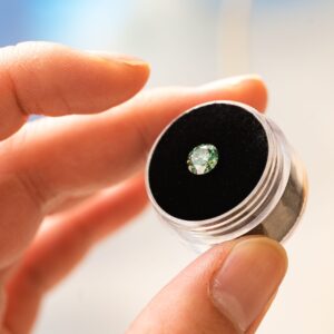 A detailed close-up of a hand holding a polished diamond in a container, showcasing its brilliance.