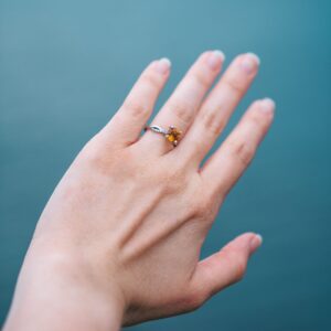 Close-up of a citrine engagement ring on a woman's hand against a blue background.